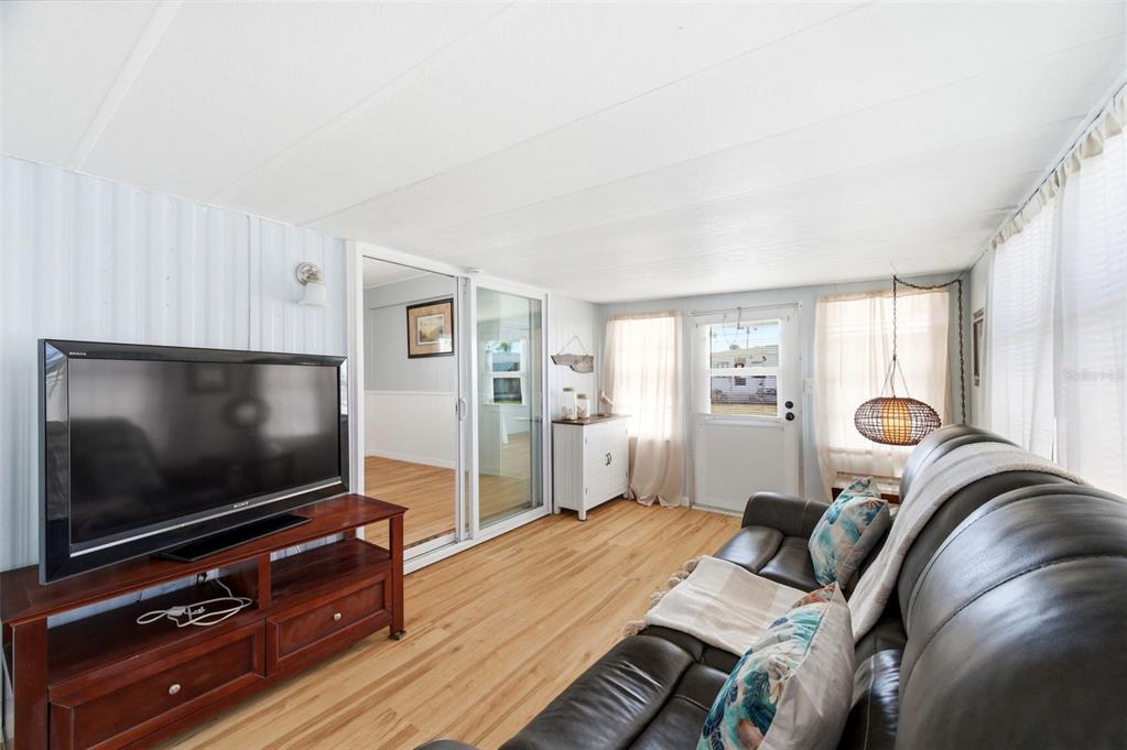 A living room with light wood flooring, a dark leather sofa, and a television console — 10913 LIBERTY DRIVE, PORT RICHEY, FL