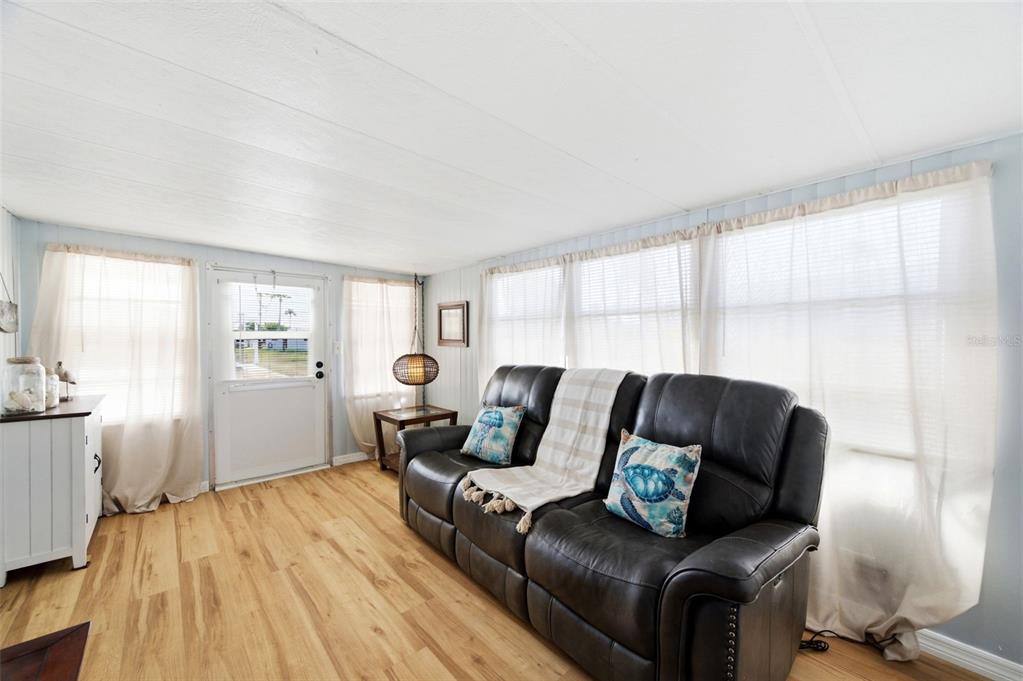 A living room features light wood flooring, a dark leather sofa, and white curtains — 10913 LIBERTY DRIVE, PORT RICHEY, FL
