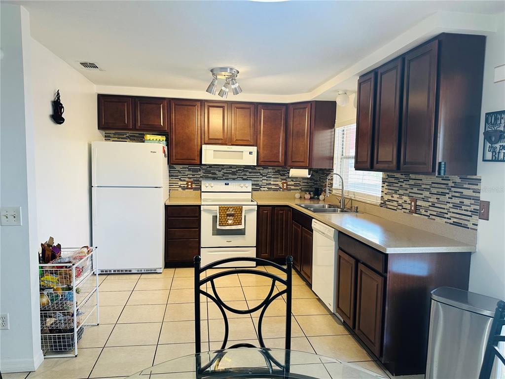 A kitchen features dark wood cabinets, white appliances, a tiled backsplash, and light-colored floor tiles — 640 E CUMMINGS STREET, LAKE ALFRED, FL