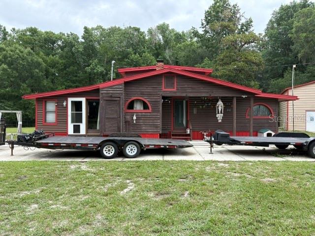 A dark brown wooden house with red trim features two flatbed trailers parked in front — 12253 E BERRY LANE, FLORAL CITY, FL