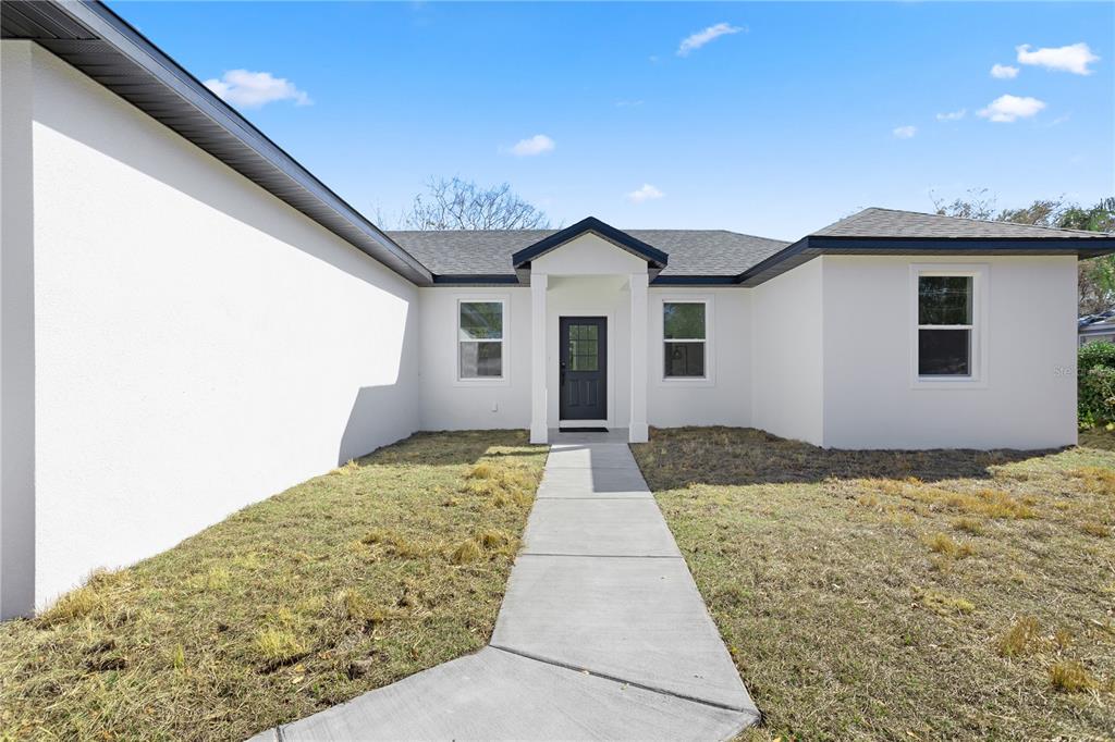 A white stucco house features a dark front door, gray roof, and a concrete walkway — 1531 OAK LANE, CASSELBERRY, FL