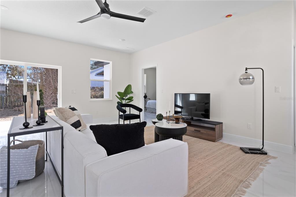 A bright living room features a white sofa, a television, and a neutral area rug — 1531 OAK LANE, CASSELBERRY, FL