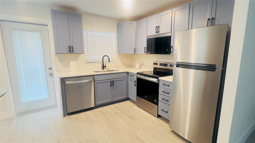 A kitchen features light blue cabinets, stainless steel appliances, and light-colored wood-look tile flooring — 4201 DES MOINES STREET NE, ST PETERSBURG, FL