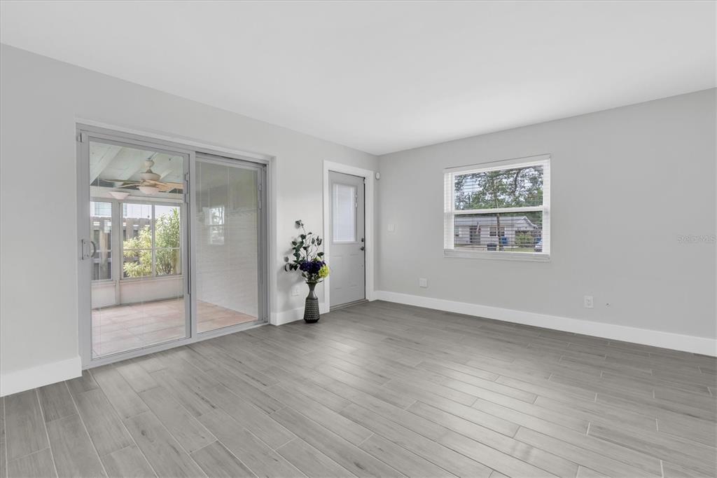 A room with light gray walls, wood-look tile flooring, a sliding glass door, and a window — 4201 DES MOINES STREET NE, ST PETERSBURG, FL