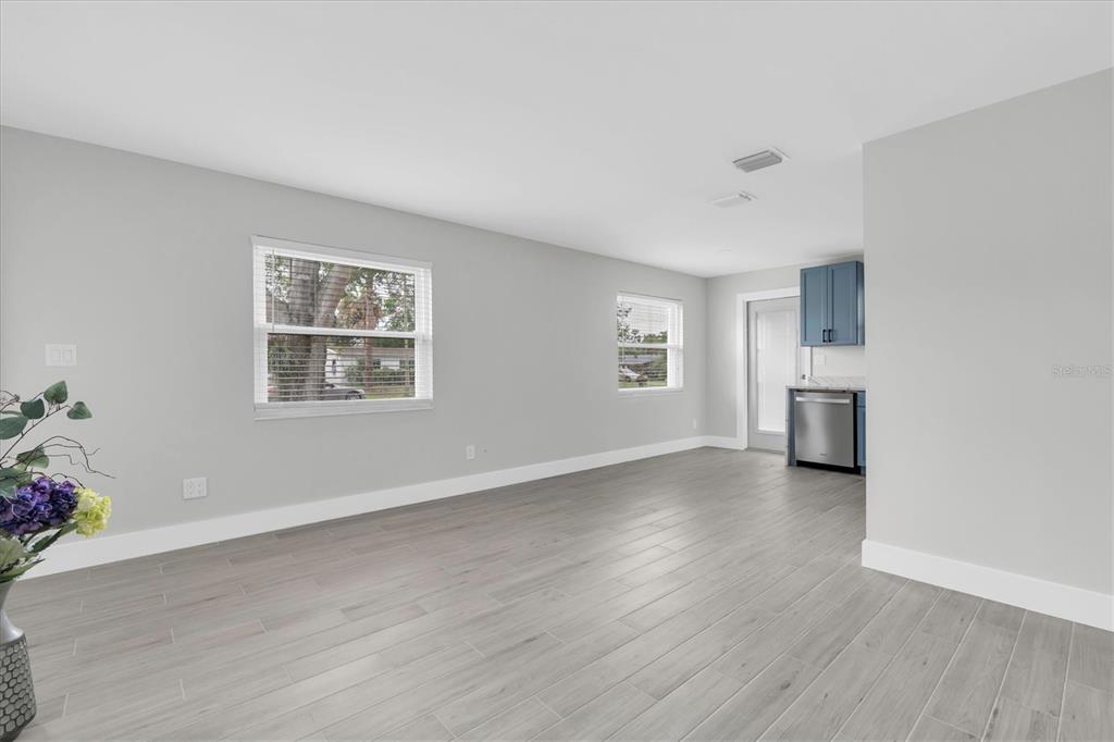 A bright, empty room with light gray walls, wood-look tile flooring, and a kitchen area — 4201 DES MOINES STREET NE, ST PETERSBURG, FL