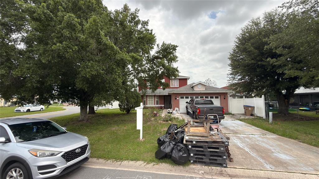 A two-story house with a red exterior, a two-car garage, and a driveway with debris — 187 PINEWOOD CIRCLE, KISSIMMEE, FL