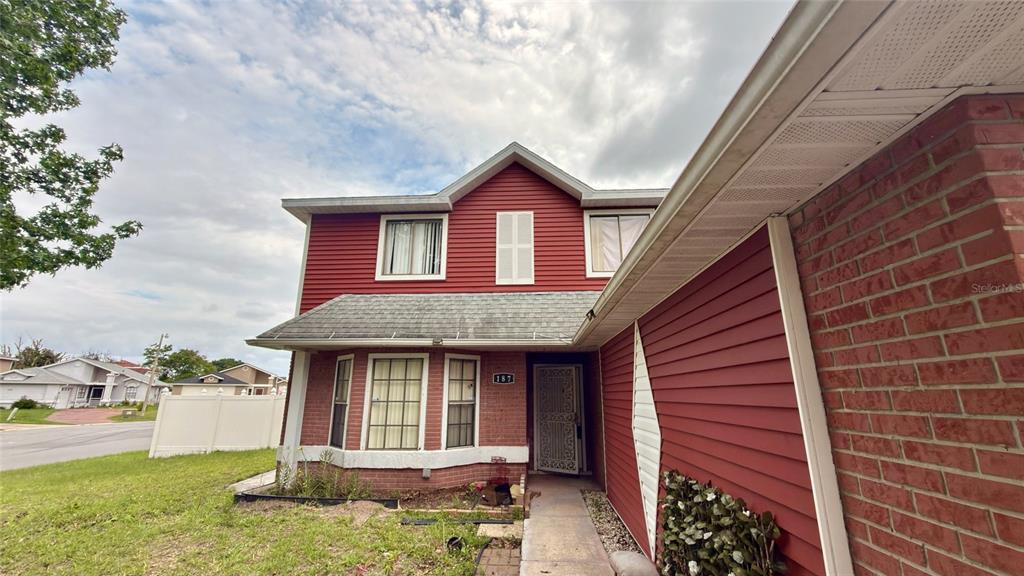 A two-story house features red siding, brick accents, a gabled roof, and a front entrance — 187 PINEWOOD CIRCLE, KISSIMMEE, FL