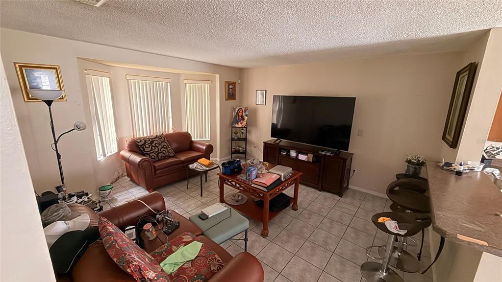 A living room features tile flooring, a leather sofa, a coffee table, and a television — 187 PINEWOOD CIRCLE, KISSIMMEE, FL