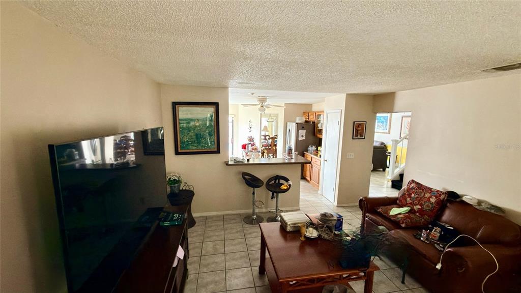 A living room with tile floors, a brown leather sofa, and a breakfast bar kitchen — 187 PINEWOOD CIRCLE, KISSIMMEE, FL
