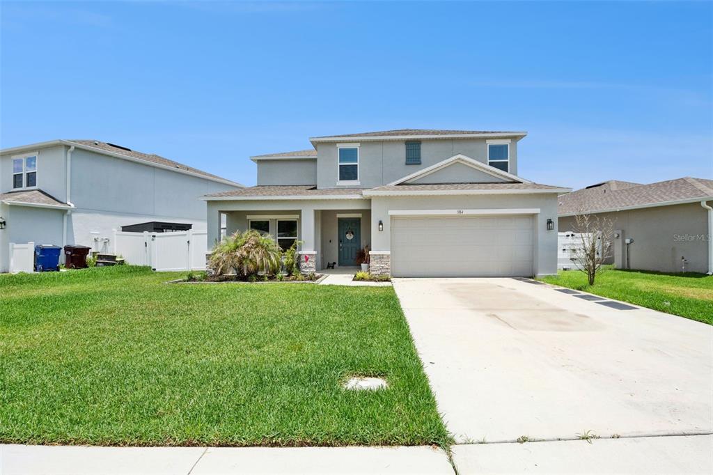 A two-story suburban house features a light gray exterior, a two-car garage, and a lawn — 584 PINK IBIS BEND, ST CLOUD, FL