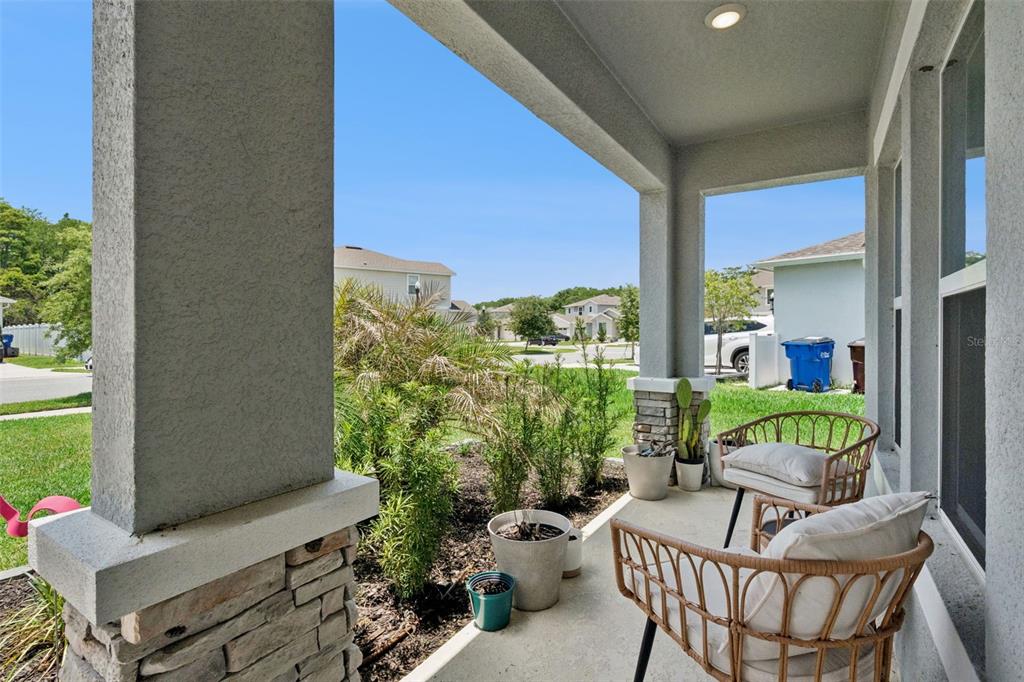 A covered front porch features stone-based columns, potted plants, and two wicker chairs — 584 PINK IBIS BEND, ST CLOUD, FL
