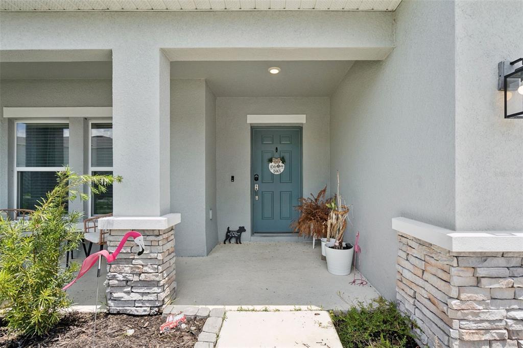A covered front porch features a blue door, stone pillars, and decorative lawn ornaments — 584 PINK IBIS BEND, ST CLOUD, FL