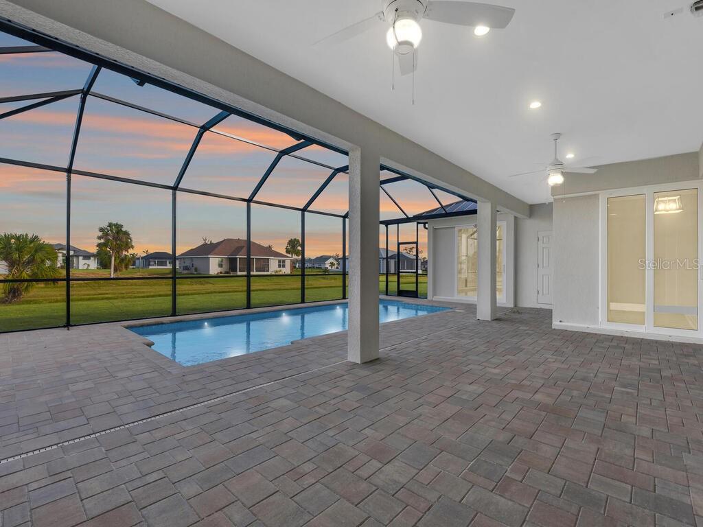 A swimming pool with a paved deck is enclosed by a screened lanai overlooking a yard — 241 ROTONDA BOULEVARD S, ROTONDA WEST, FL