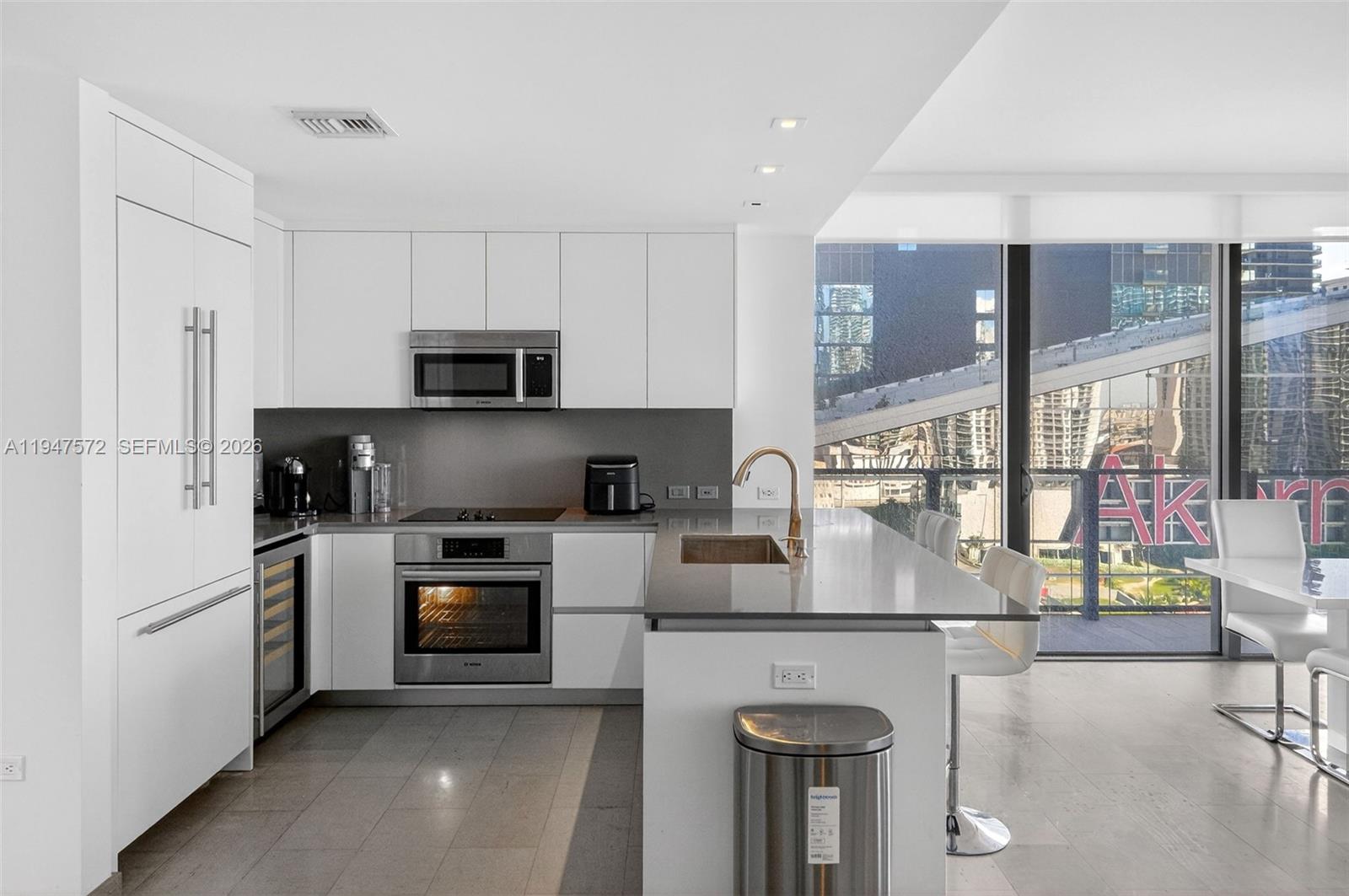 A modern kitchen features white cabinetry, stainless steel appliances, a center island, and floor-to-ceiling windows — 68 SE 6th St # 1702, Miami FL 33131, MIAMI, FL