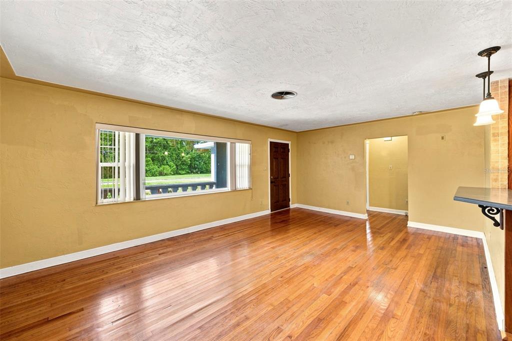 A living room with hardwood floors, yellow walls, a large window, and a dark door — 4310 DR MARTIN LUTHER KING JR STREET S, ST PETERSBURG, FL