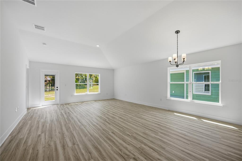 An empty room with light wood-look flooring, white walls, a vaulted ceiling, and a chandelier — 16822 NW 178TH TERRACE, ALACHUA, FL