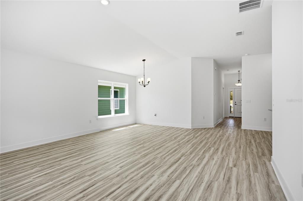 A bright, empty room features light wood-look flooring, white walls, and a hanging chandelier — 16822 NW 178TH TERRACE, ALACHUA, FL