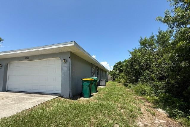 The side view of a house shows a garage door, two trash bins, and landscaping — 3098 BEACON DRIVE, PORT CHARLOTTE, FL