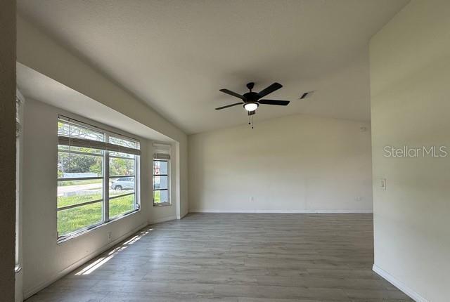 A living room with light wood-look flooring, a ceiling fan, and large windows — 3098 BEACON DRIVE, PORT CHARLOTTE, FL