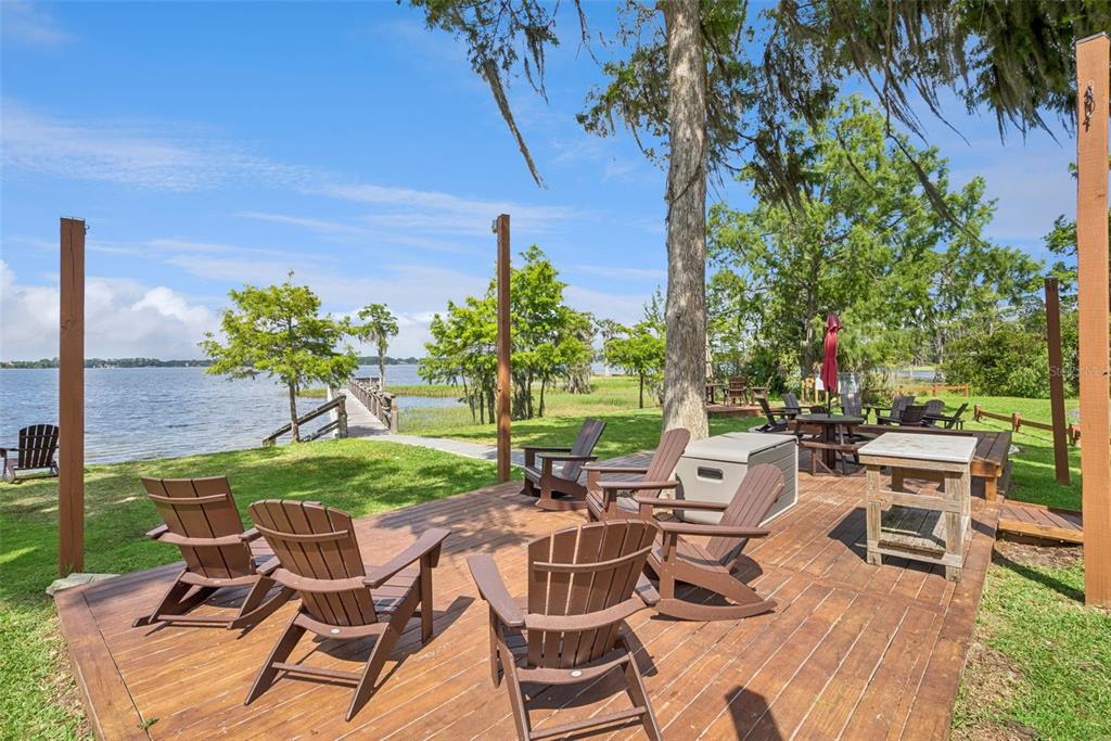 A wooden deck with Adirondack chairs overlooks a lake with a wooden pier — 10490 WISCANE AVENUE, ORLANDO, FL