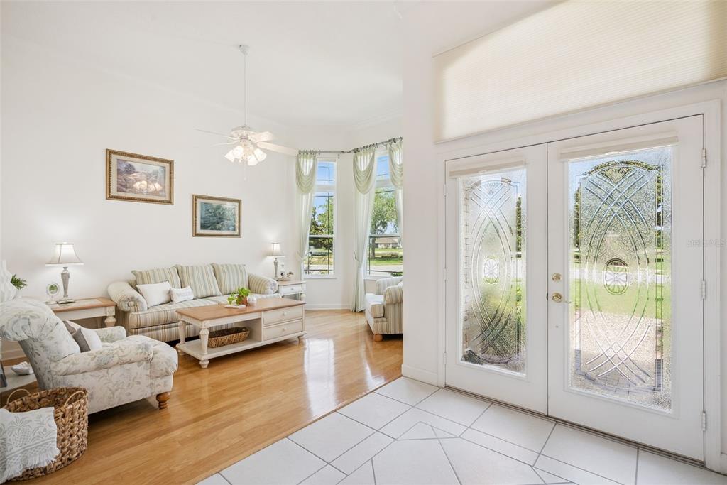 A bright living room features hardwood floors, a ceiling fan, and double glass-paneled entry doors — 10490 WISCANE AVENUE, ORLANDO, FL