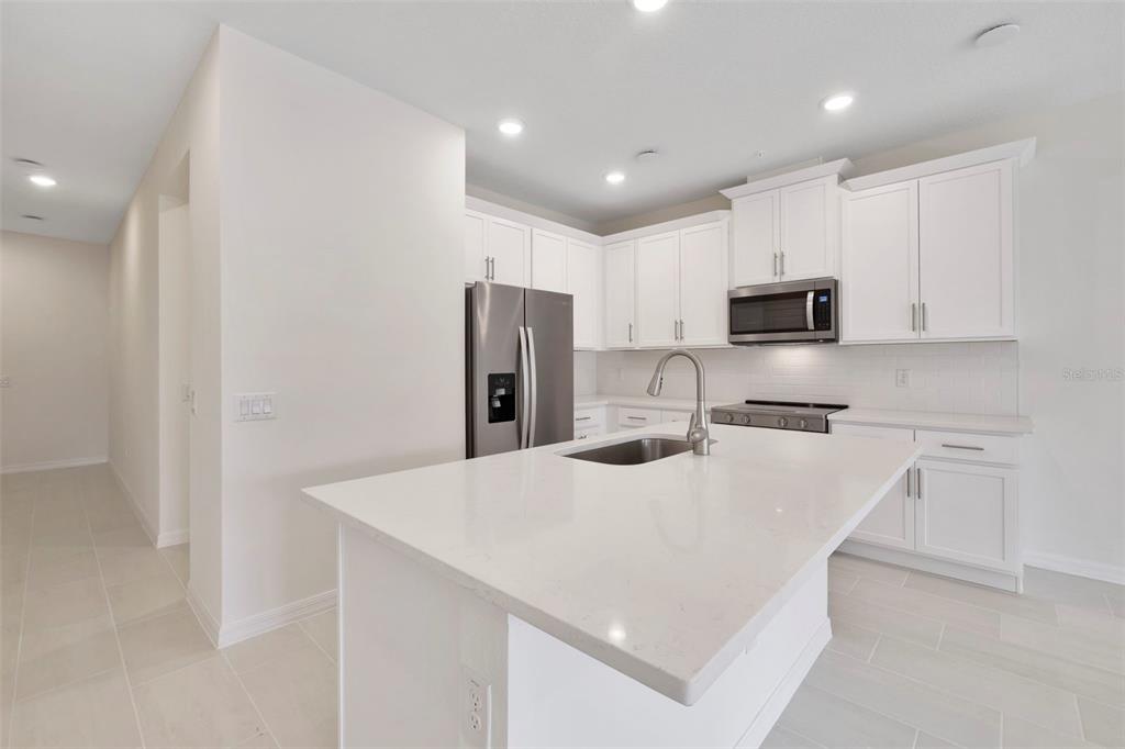 A modern kitchen features white cabinets, stainless steel appliances, and a large quartz-topped island — 543 SOUTHERN EDGE WAY, SANFORD, FL