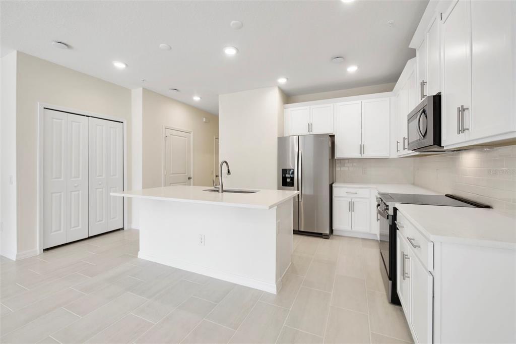 A modern kitchen features white cabinets, stainless steel appliances, a center island, and light tile flooring — 543 SOUTHERN EDGE WAY, SANFORD, FL
