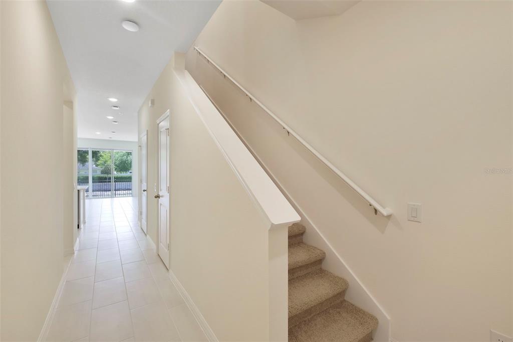 A hallway with tile flooring leads to a glass door, featuring carpeted stairs with railings — 543 SOUTHERN EDGE WAY, SANFORD, FL
