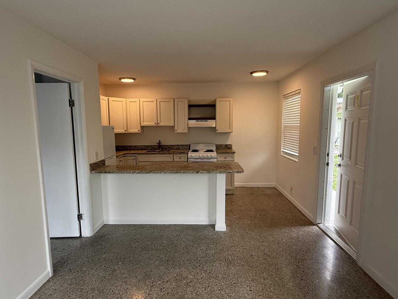 A kitchen features light-colored cabinets, granite countertops, a white stove, and speckled concrete flooring — 1118 N H Street # 4, FL 33460, FL