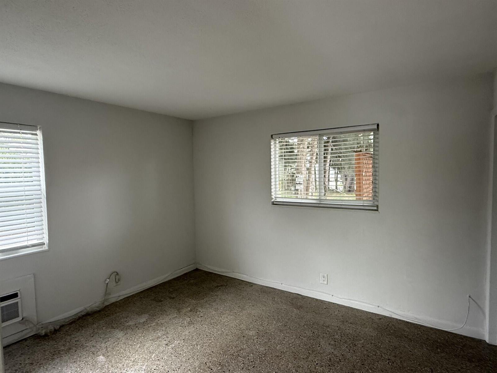 An empty room with white walls, two windows with blinds, and speckled flooring — 1118 N H Street # 4, FL 33460, FL