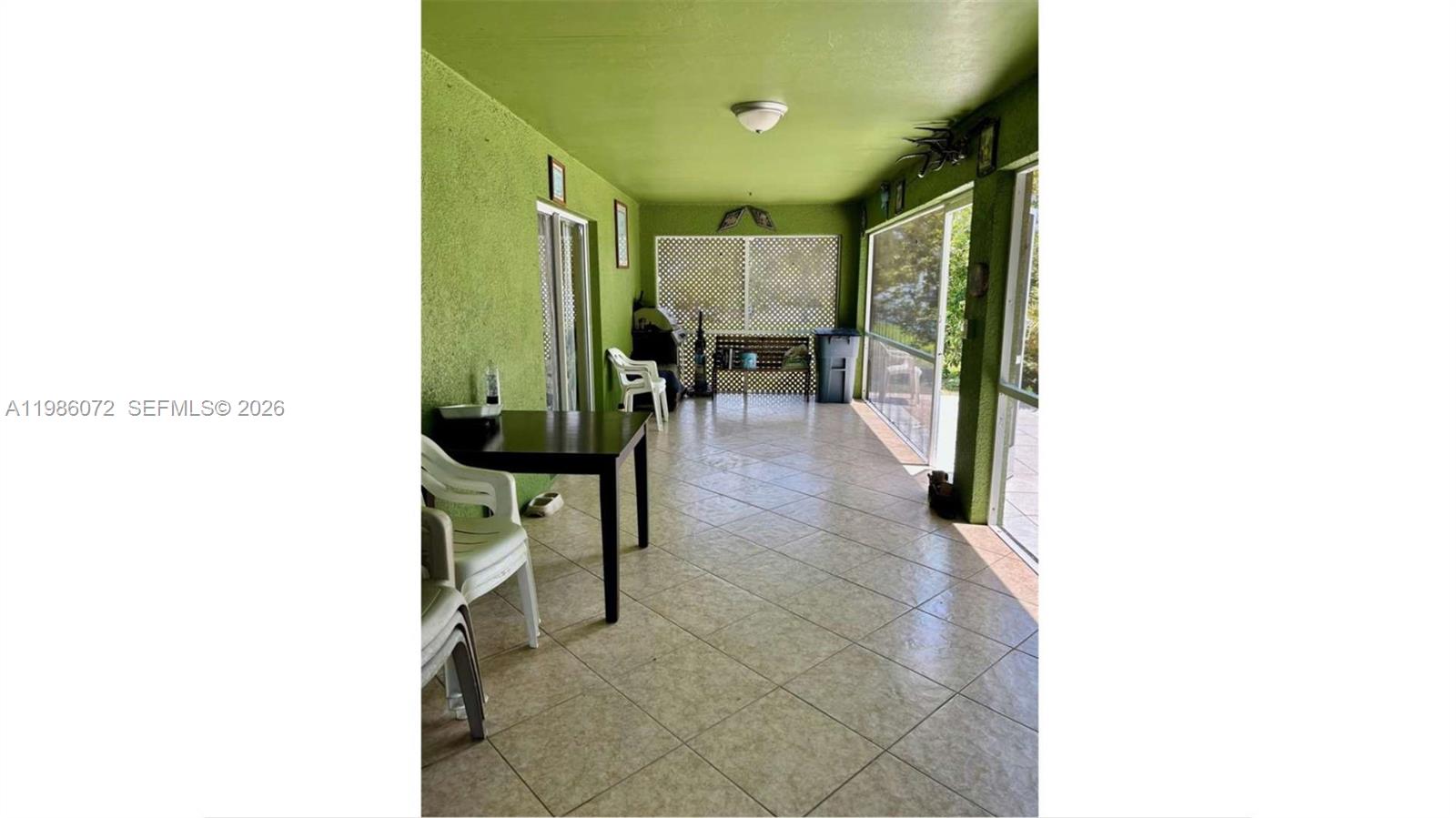 A covered patio features green textured walls, tiled flooring, and large screened windows — 1122 MCKINLEY AVE, Lehigh Acres FL 33972, LEHIGH ACRES, FL