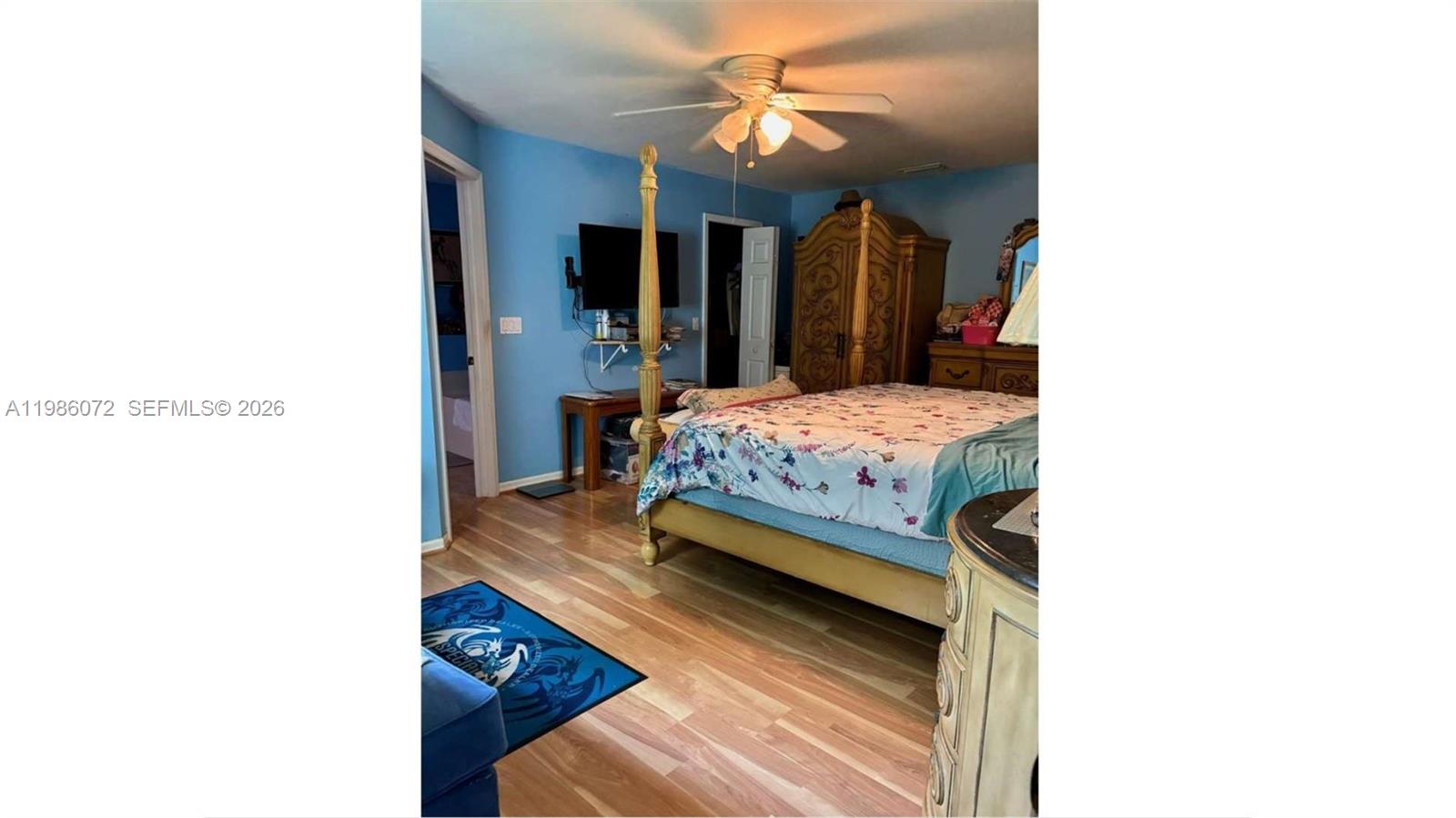 A bedroom features blue walls, a four-poster bed, wood flooring, and a ceiling fan — 1122 MCKINLEY AVE, Lehigh Acres FL 33972, LEHIGH ACRES, FL