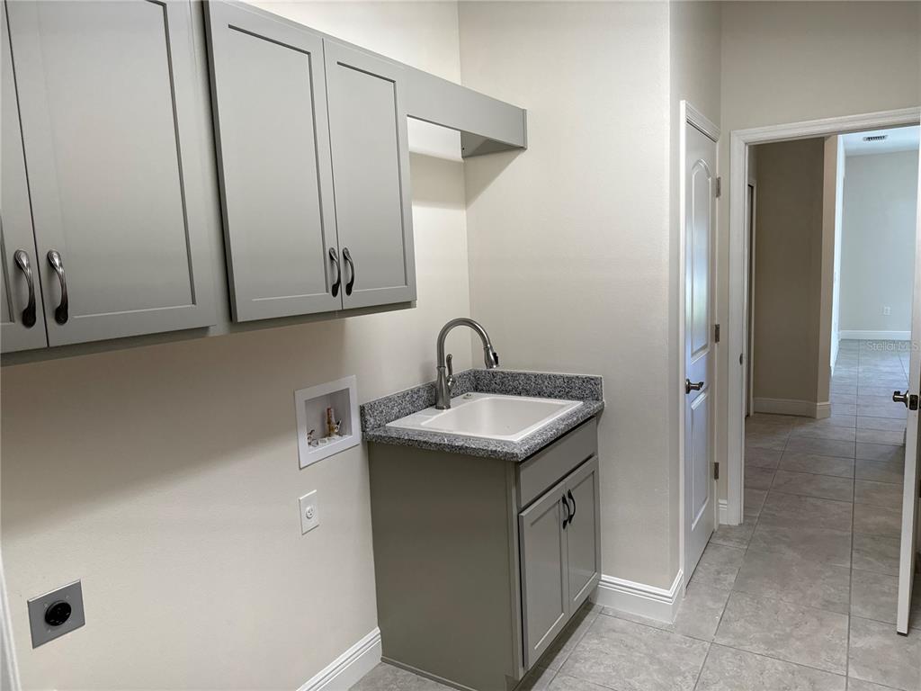 A laundry room features grey cabinets, a utility sink with a granite countertop, and tile flooring — 4420 MIDLAND STREET, NORTH PORT, FL