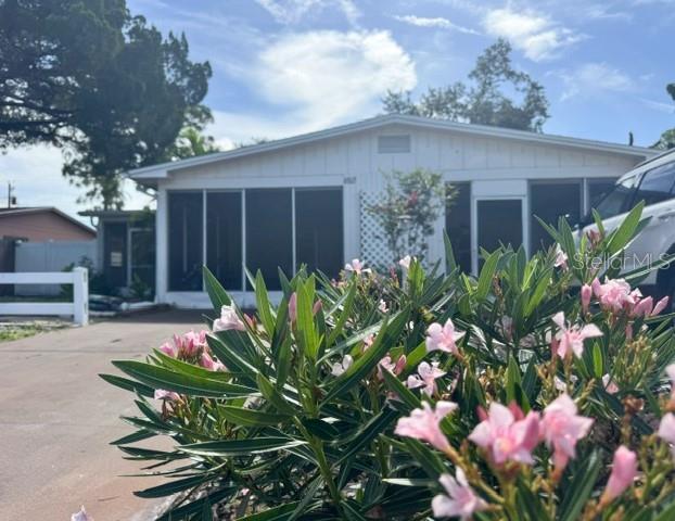 A white single-story house with a screened-in porch is viewed behind a blooming oleander bush — 4805 21ST STREET W, BRADENTON, FL