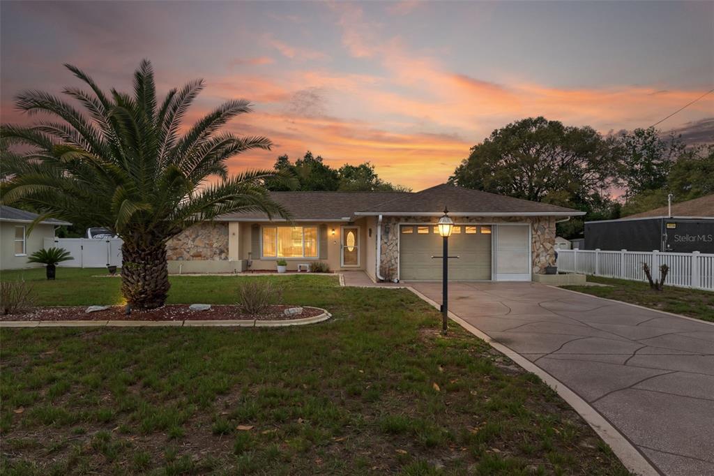 A single-story house with a stone facade, a palm tree, and a concrete driveway at sunset — 3217 ABELINE ROAD, SPRING HILL, FL