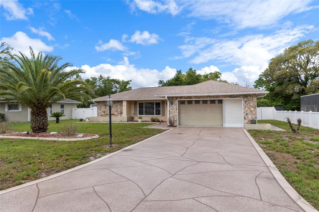 A single-story house with a stone facade, a paved driveway, and a large palm tree — 3217 ABELINE ROAD, SPRING HILL, FL