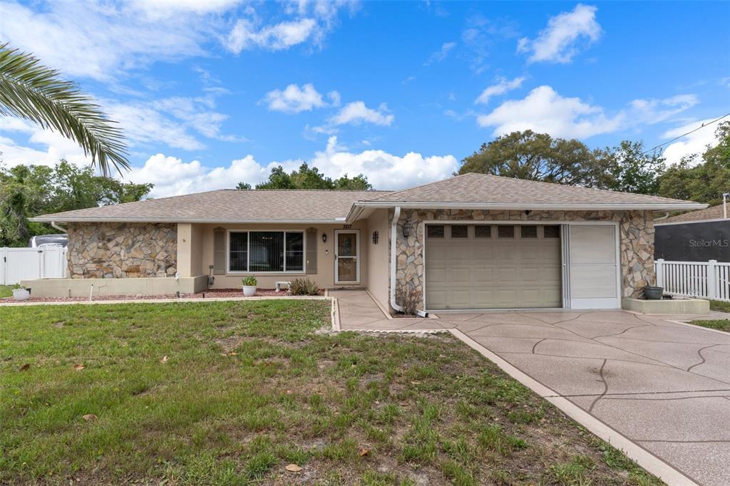 A single-story house with a stone facade, a tan garage door, and a concrete driveway — 3217 ABELINE ROAD, SPRING HILL, FL