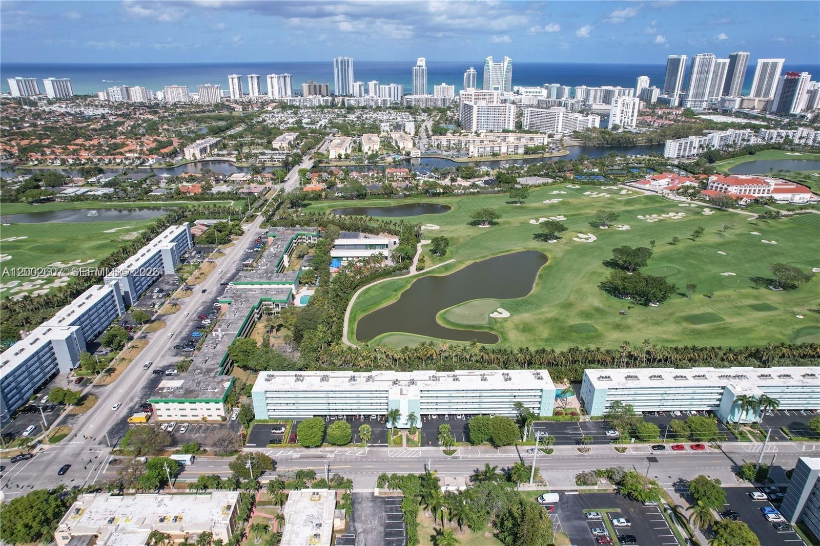 An aerial view shows apartment buildings situated next to a golf course and coastal city — 700 NE 14th Ave # 407, Hallandale Beach FL 33009, HALLANDALE BEACH, FL