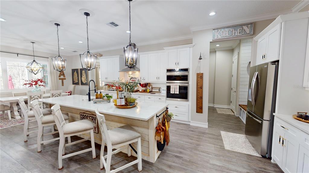 A bright kitchen features white cabinetry, a large island with seating, and stainless steel appliances — 4801 MAJESTIC HILLS LOOP, BROOKSVILLE, FL