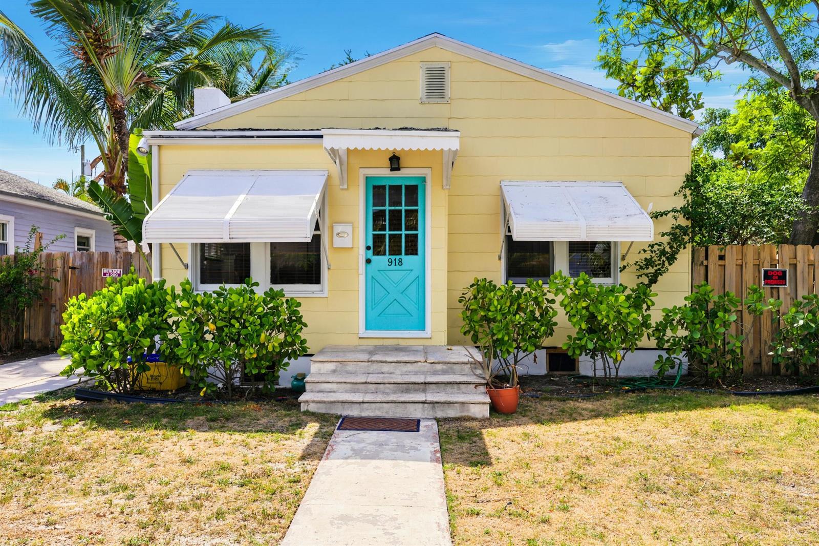 A yellow cottage with a turquoise front door, white awnings, and a concrete walkway — 918 N K Street, FL 33460, FL