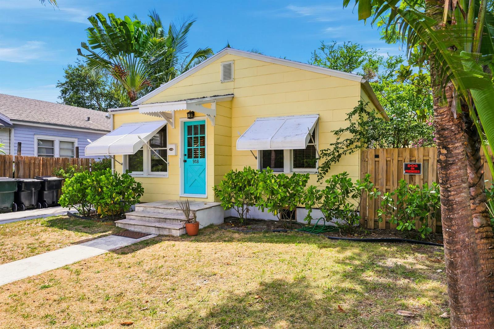 A yellow single-story house with a turquoise door, white awnings, and a wooden fence — 918 N K Street, FL 33460, FL