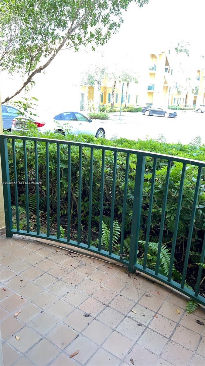 A green metal railing borders a tiled patio overlooking a parking lot and landscaping — 7350 NW 114th Ave # 103, Doral FL 33178, DORAL, FL