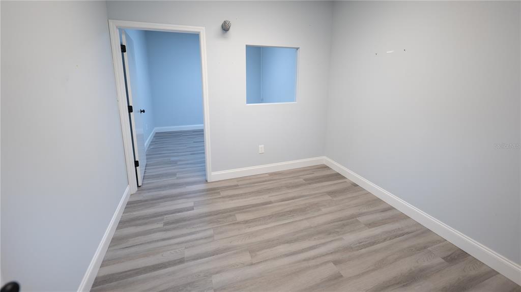 An empty room with light blue walls, wood-look flooring, and a square interior window — 1209 TECH BOULEVARD UNIT 211, TAMPA, FL