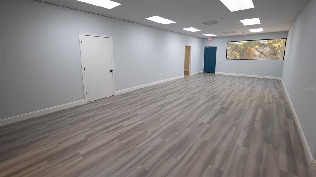 An empty office room features light gray walls, wood-look flooring, and a blue exit door — 1209 TECH BOULEVARD UNIT 211, TAMPA, FL