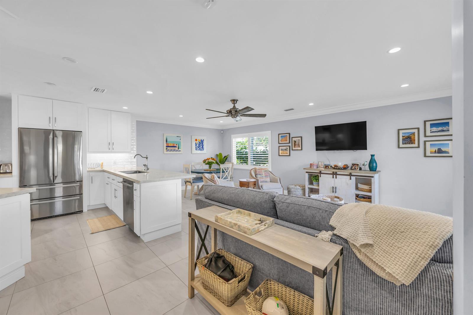 An open-concept living room and kitchen featuring a gray sofa, white cabinetry, and tile flooring — 234 Seabreeze Circle, Jupiter FL 33477, JUPITER, FL