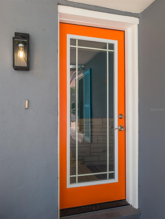 A bright orange front door with a glass panel sits in a gray exterior wall — 3702 KINGSBURY, HOLIDAY, FL