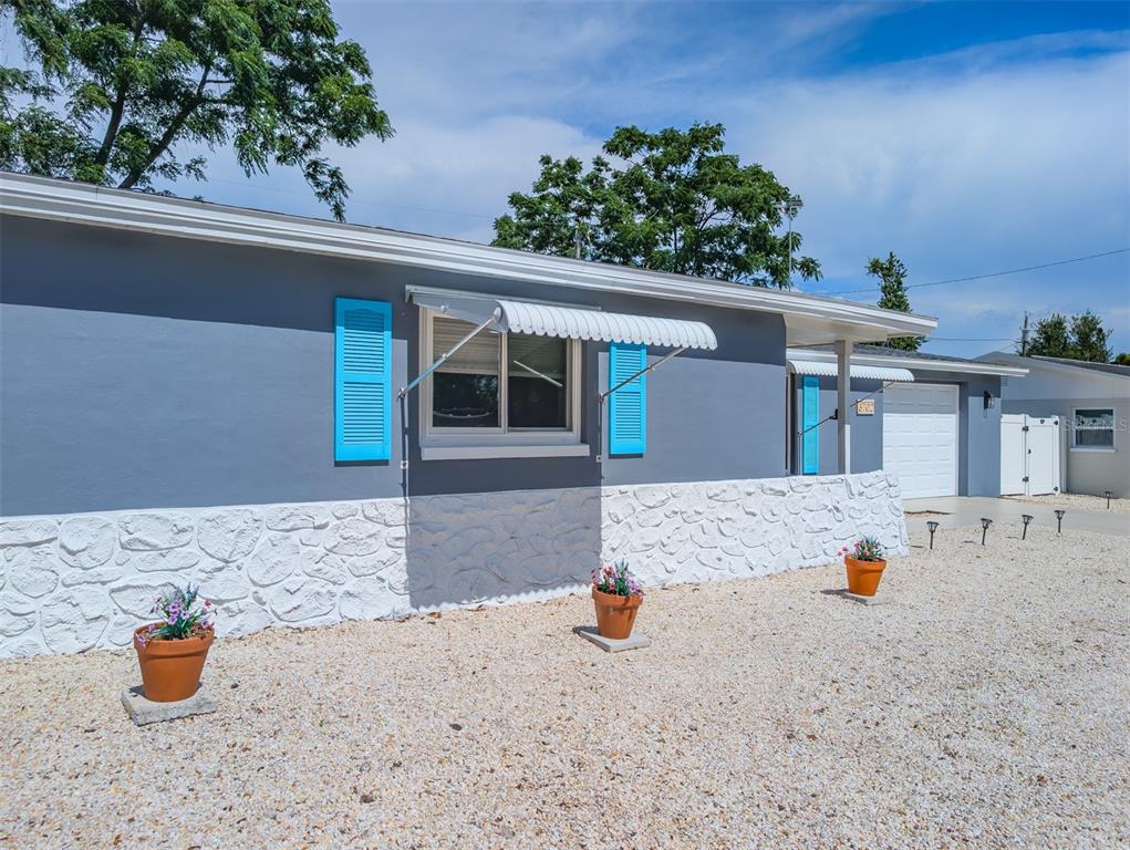 A grey house exterior features white stone siding, bright blue shutters, and three potted plants — 3702 KINGSBURY, HOLIDAY, FL