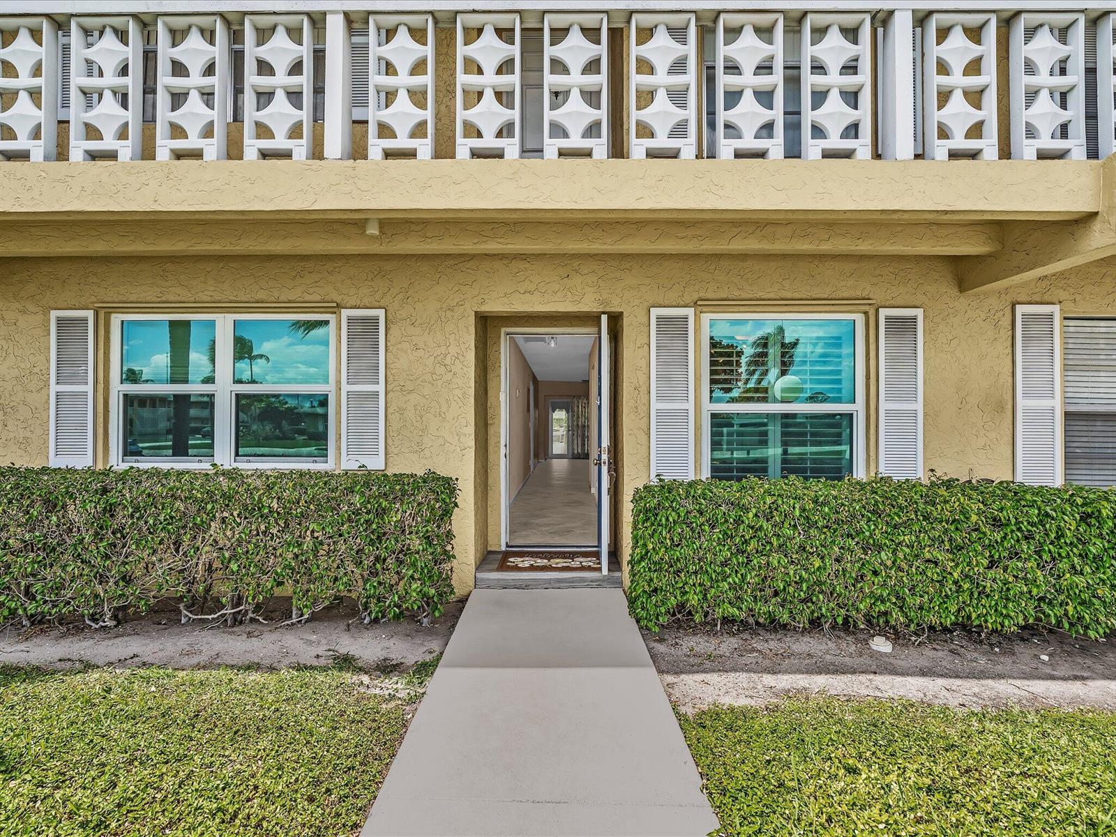 A yellow stucco building exterior features a central open doorway, windows with shutters, and hedges — 1151 Calamondin Terrace, Delray Beach FL 33445, DELRAY BEACH, FL