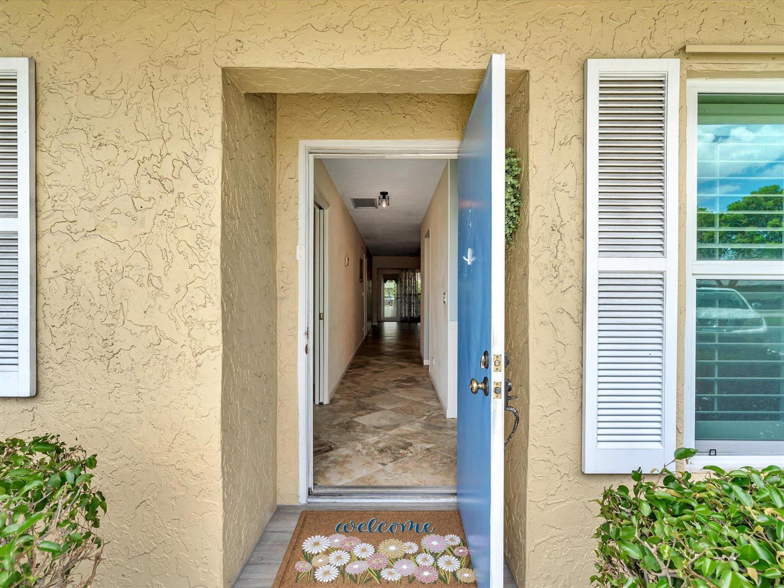 An open blue front door reveals a tiled hallway inside a beige stucco home — 1151 Calamondin Terrace, Delray Beach FL 33445, DELRAY BEACH, FL