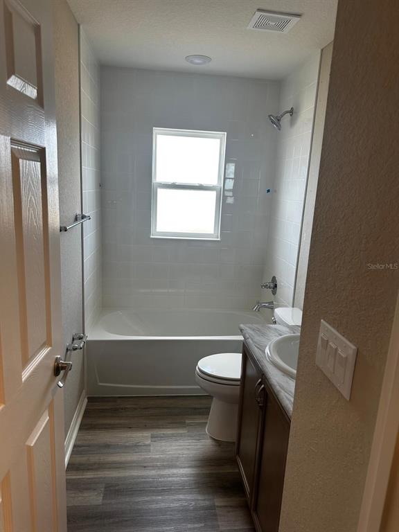 A bathroom features a white tiled tub-shower combo, a vanity, and wood-look flooring — 1391 MOUNTAIN FLOWER LANE, DAVENPORT, FL